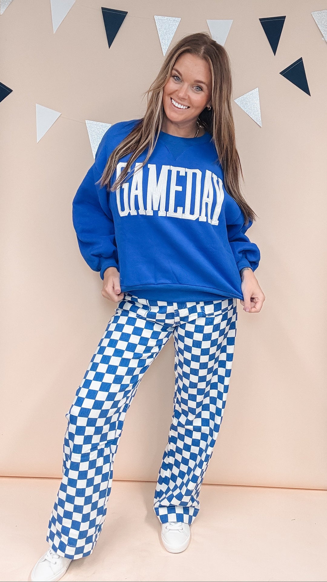 Woman wearing cobalt blue gameday sweatshirt with blue and white checkered pants on plain background
