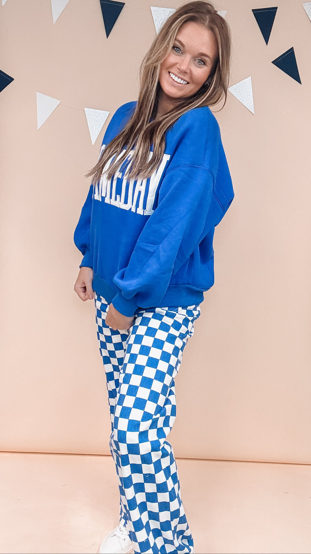 Woman wearing cobalt blue gameday sweatshirt with blue and white checker pants on plain background