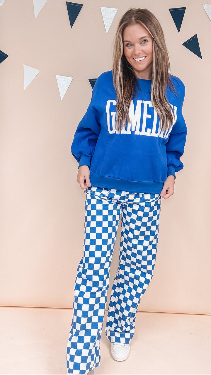 Woman wearing cobalt blue gameday sweatshirt and blue and white checker pants on plain background