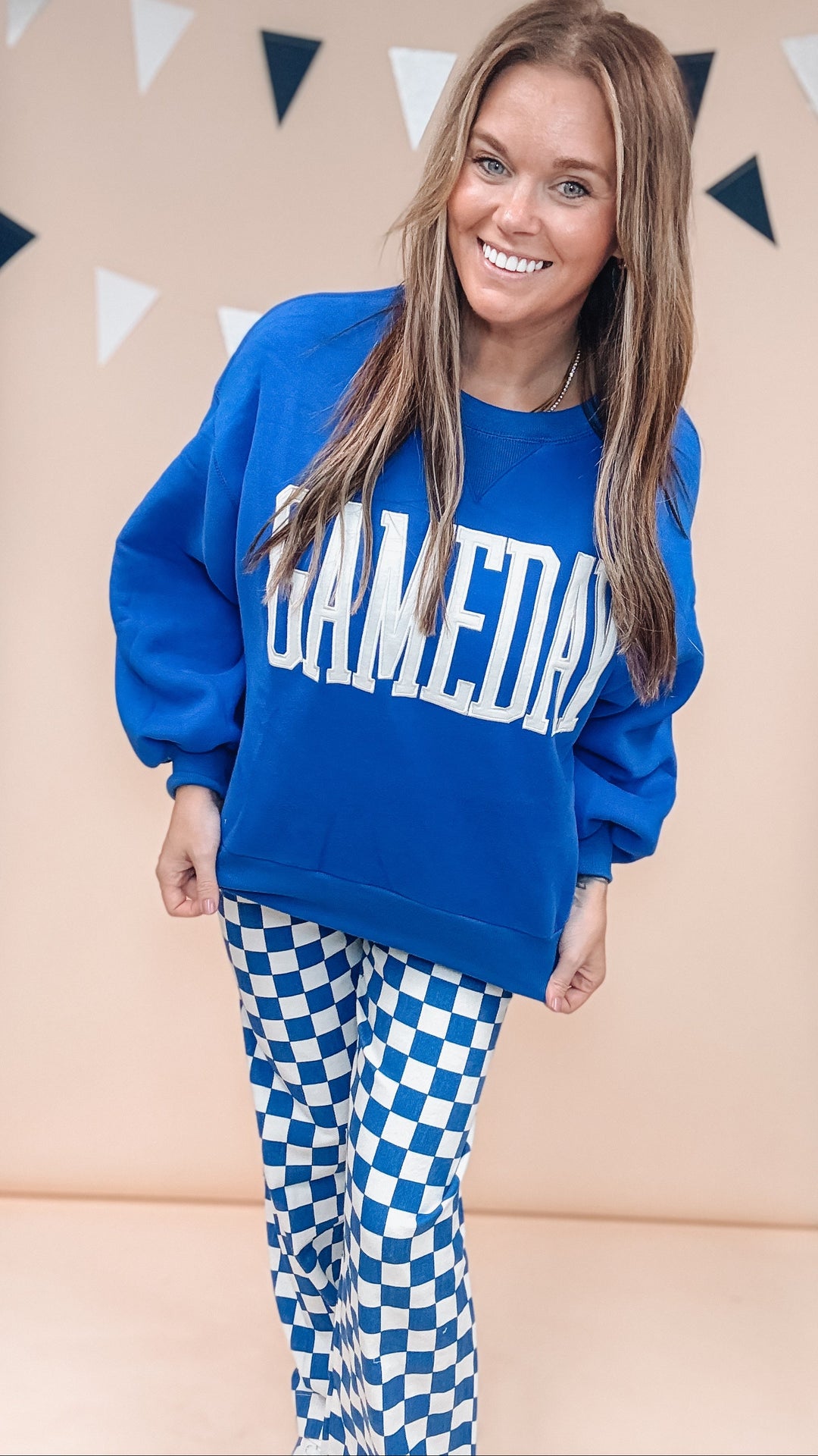 Woman wearing blue gameday sweatshirt with blue and white checker pants on plain background