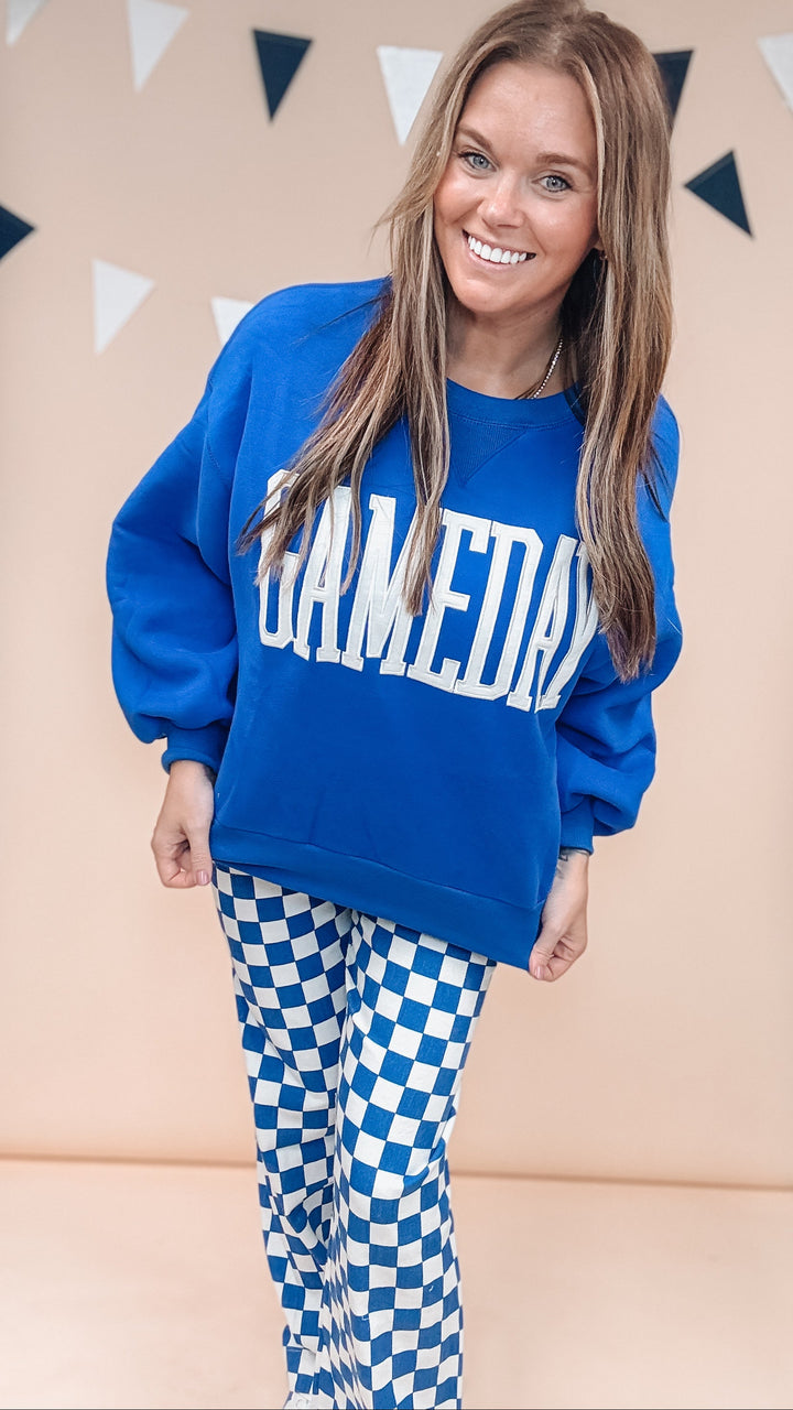 Woman wearing blue gameday sweatshirt with blue and white checker pants on plain background
