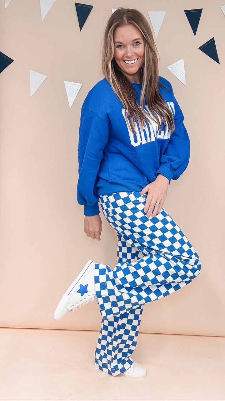 Woman wearing blue gameday sweatshirt with blue and white checker pants on plain background