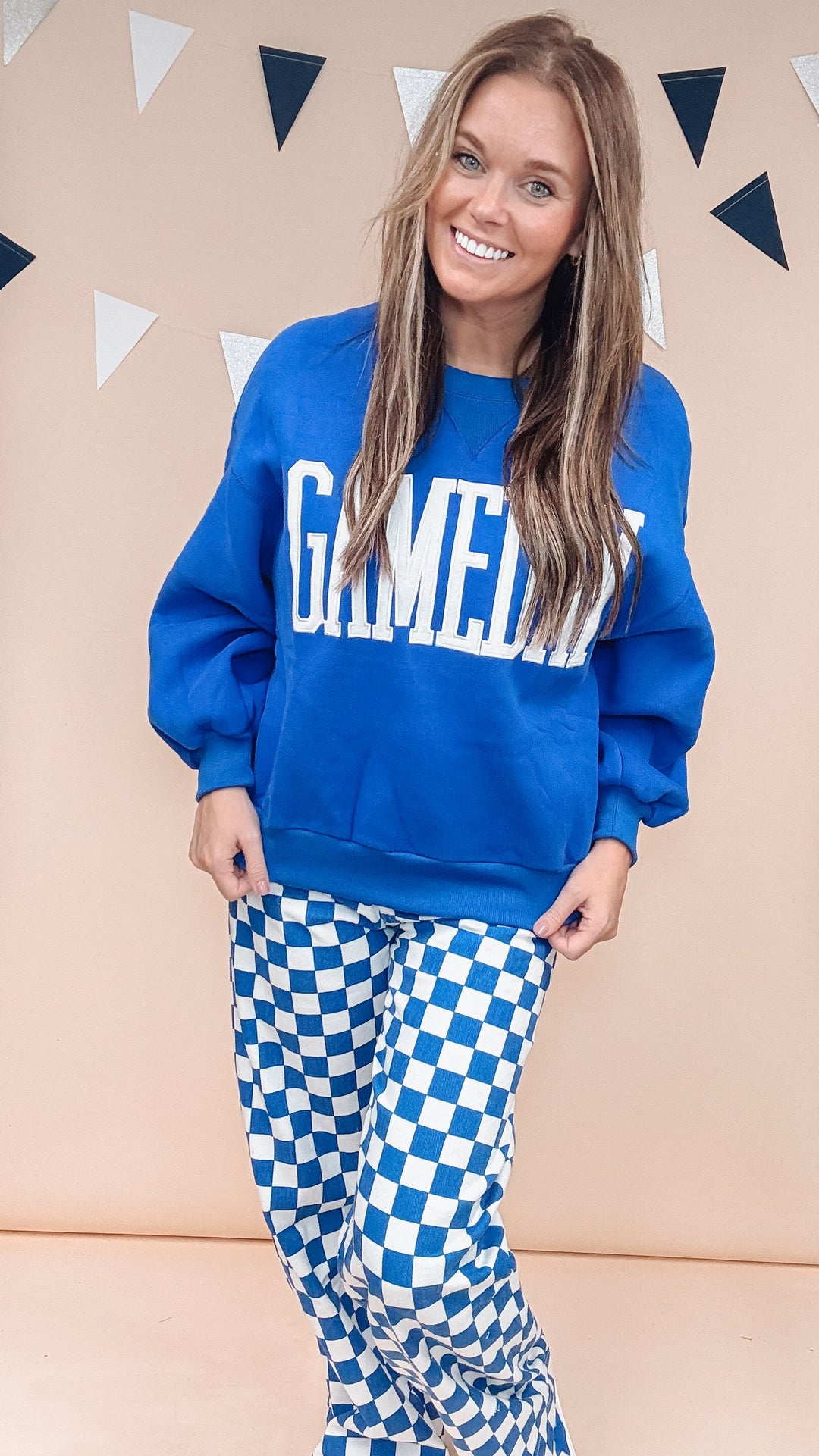 Woman wearing blue gameday sweatshirt with blue and white checker pants on plain background