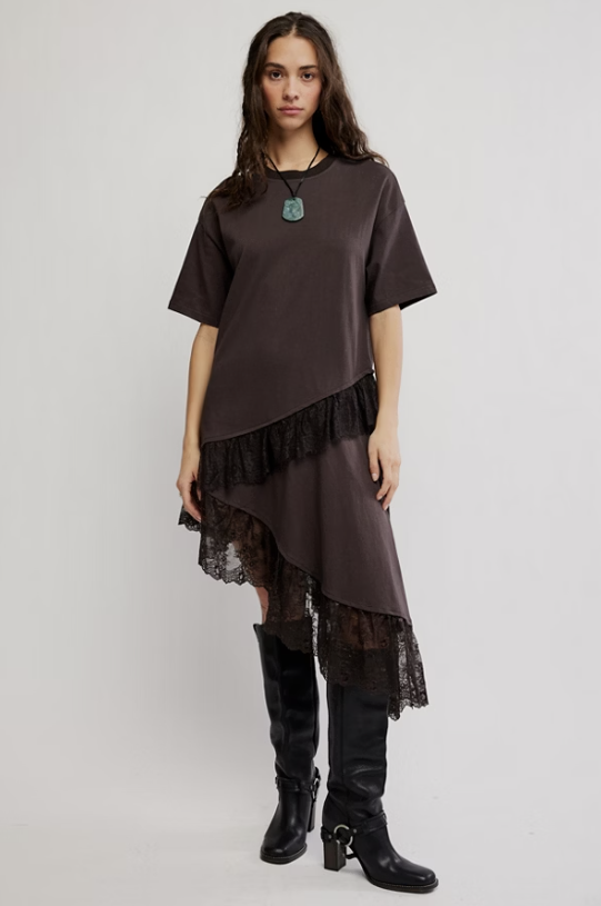 A model wearing a dark brown short-sleeve top dress with black lace ruffle trim and a black asymmetrical hem, paired with black knee-high boots, against a light gray studio background.