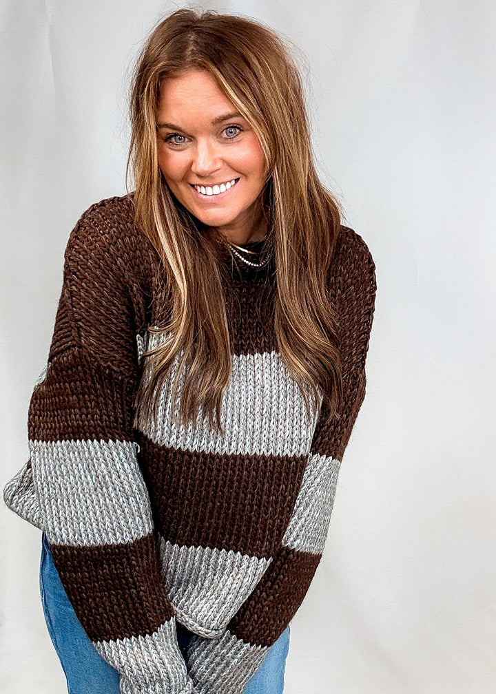 Woman wearing brown and blue stripe chunky sweater with jeans on plain background