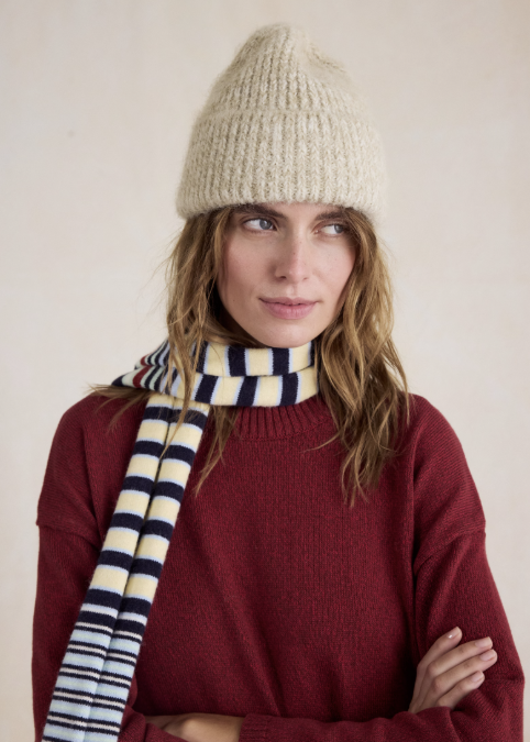 Woman wearing beige knitted beanie, striped scarf and red sweater on beige background