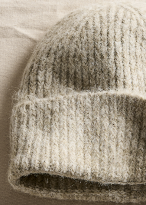 Close-up of a chunky knit beanie in a warm oatmeal beige color, showing the soft fuzzy texture of the yarn.