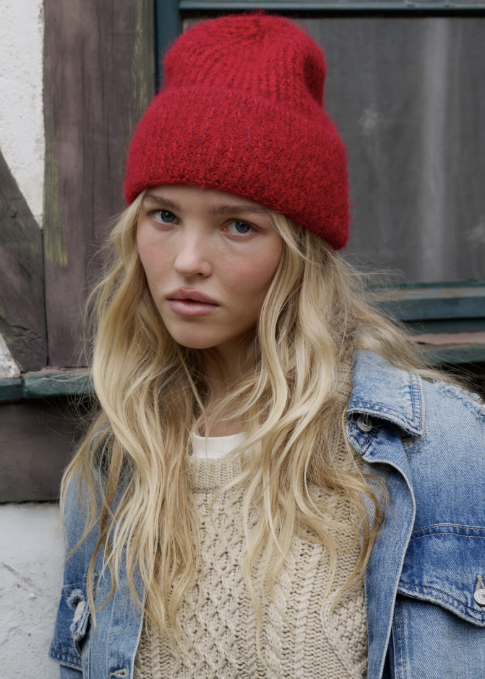 Woman wearing red knitted beanie, beige sweater and denim jacket standing outdoors