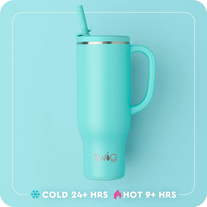 A mint green Swig vacuum-insulated travel tumbler with a matching handle and straw lid, shown against a matching light blue background with product feature text at the bottom.