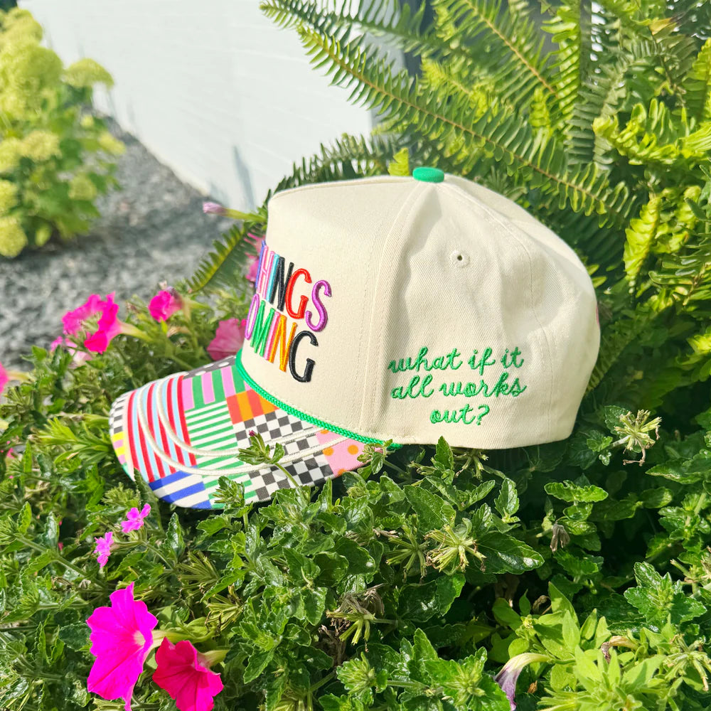 Beige cap with colorful text and patterns on a green plant background
