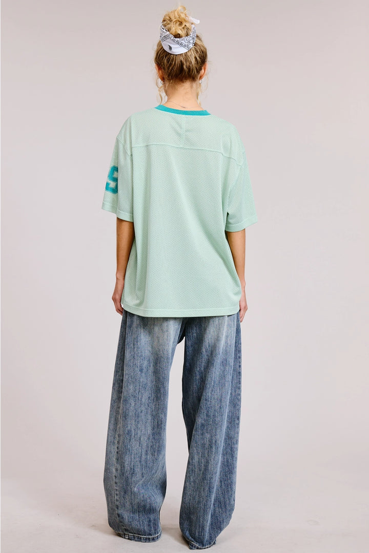 Person wearing a light green oversized t-shirt and blue jeans on a plain background