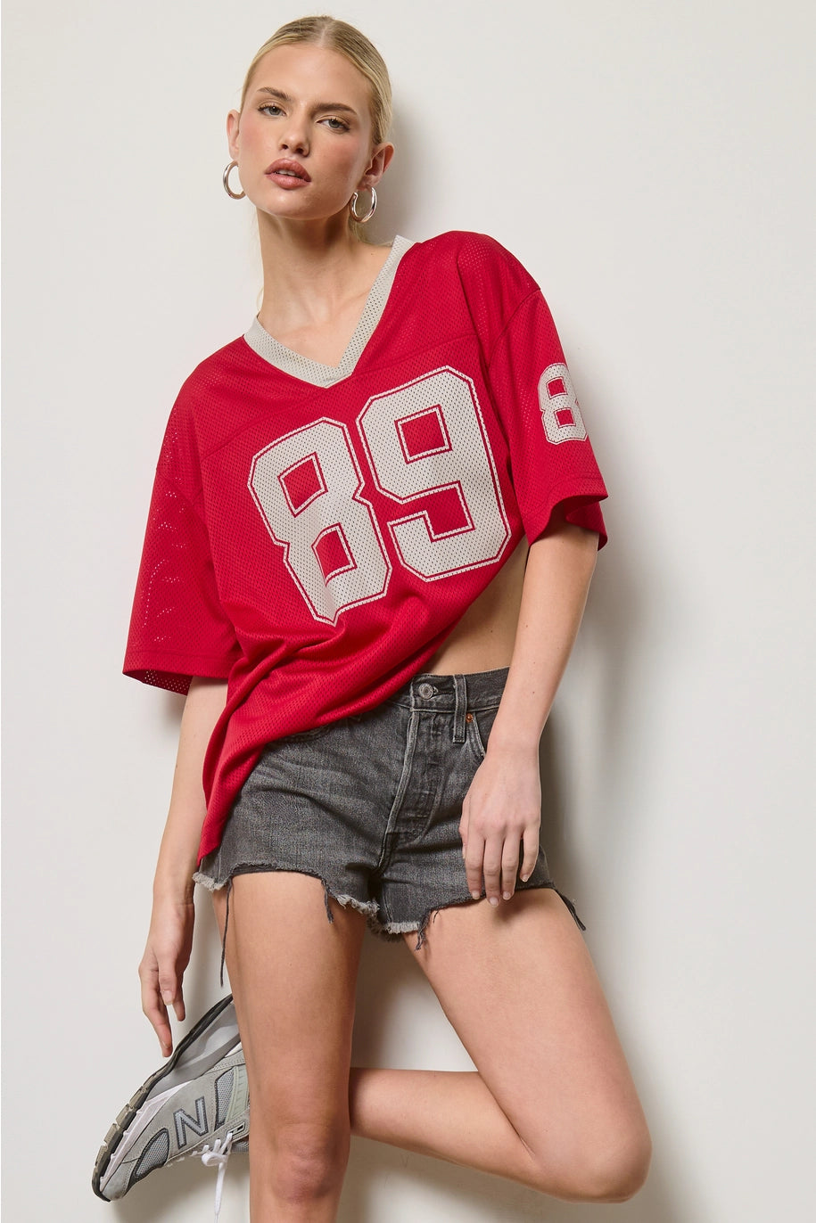 Woman wearing a red sports jersey with the number 89 on a plain background