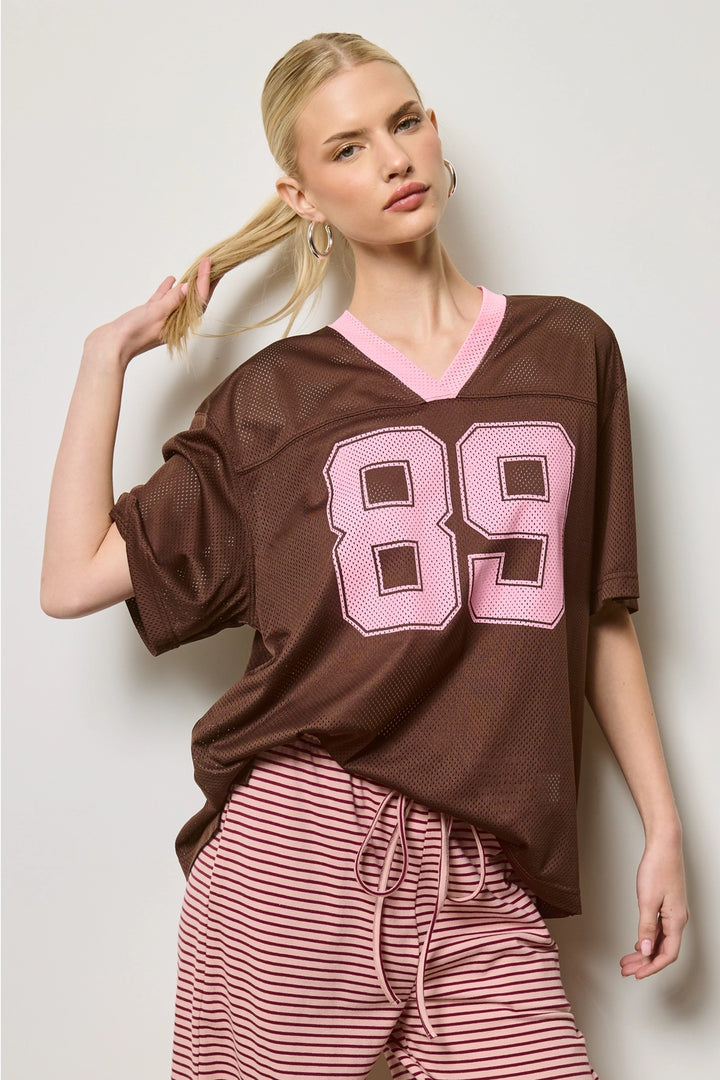 Woman wearing a brown jersey with pink number 89 and pink striped pants on a white background