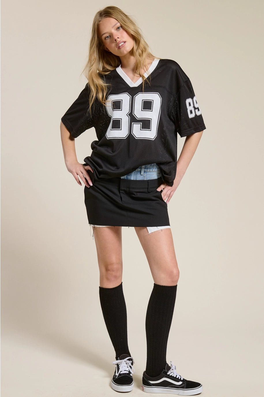 Woman wearing a black sports jersey with the number 89 on a beige background