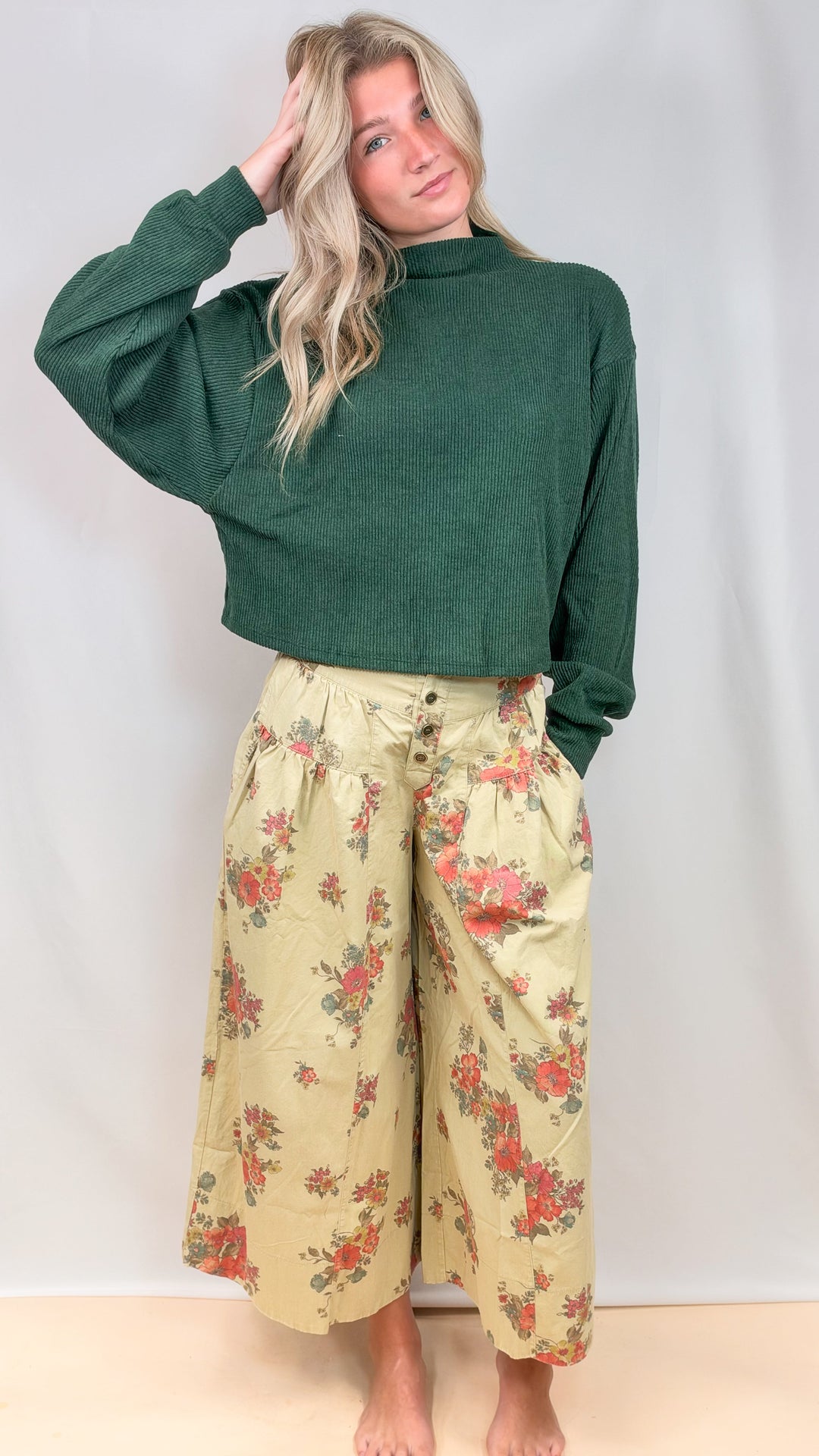 Woman wearing green mock neck sweater with floral pants on plain background