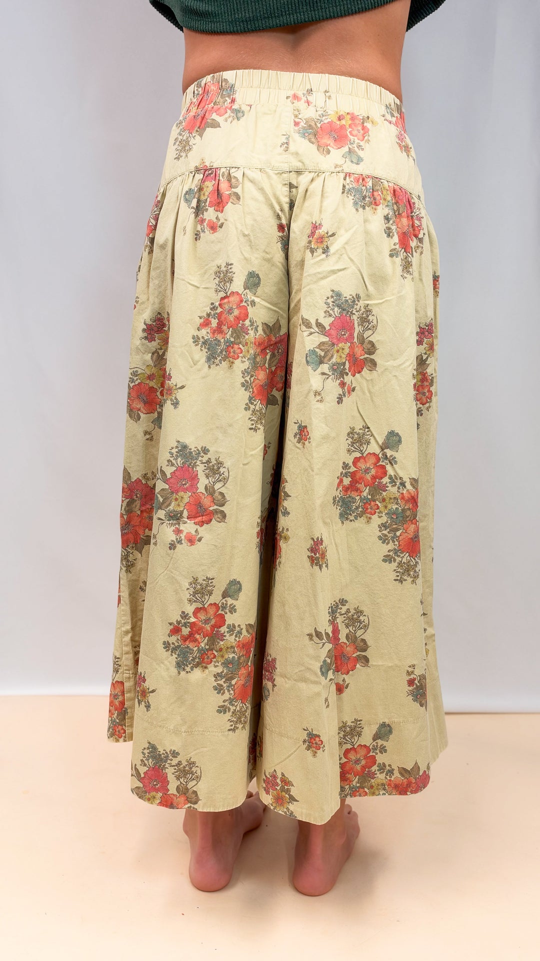 Woman shown from back view wearing floral pants on plain background
