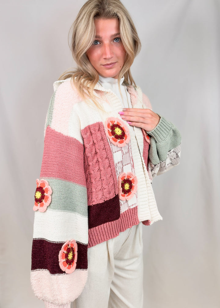 Woman wearing crochet knit cardigan with floral and lace details on plain background
