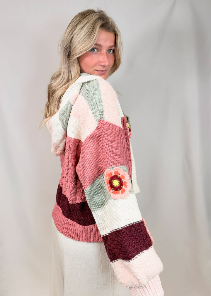 Woman shown from side view wearing crochet knit cardigan with floral details on plain background