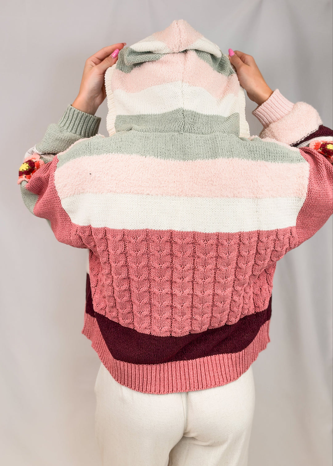 Woman shown from back view wearing crochet knit cardigan with hood on plain background