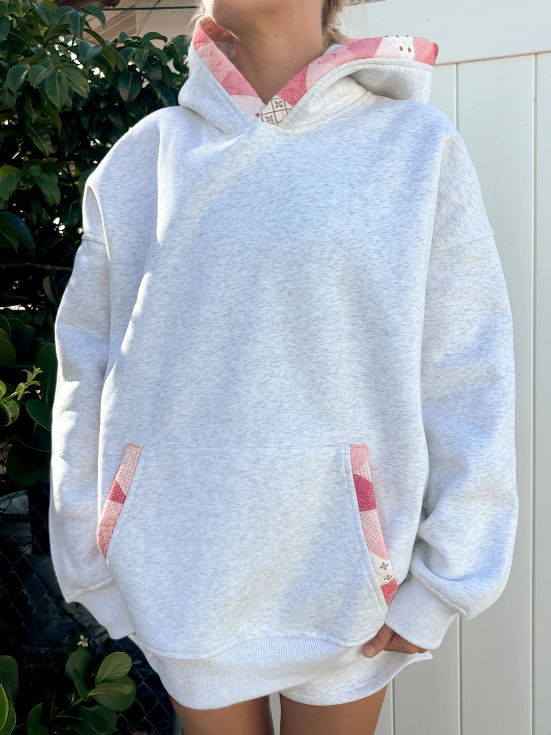 Person wearing grey hoodie with pink patchwork standing outdoors