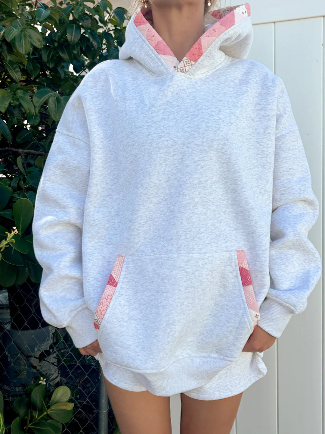 Person wearing grey hoodie with pink patchwork standing outdoors