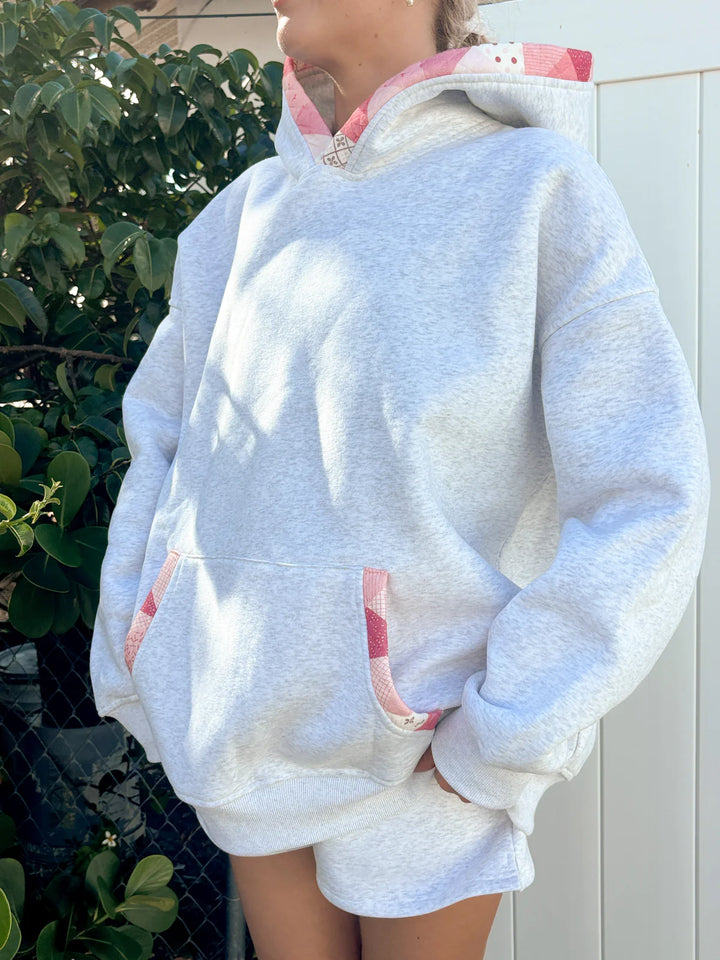 Person wearing grey hoodie with pink patchwork standing outdoors