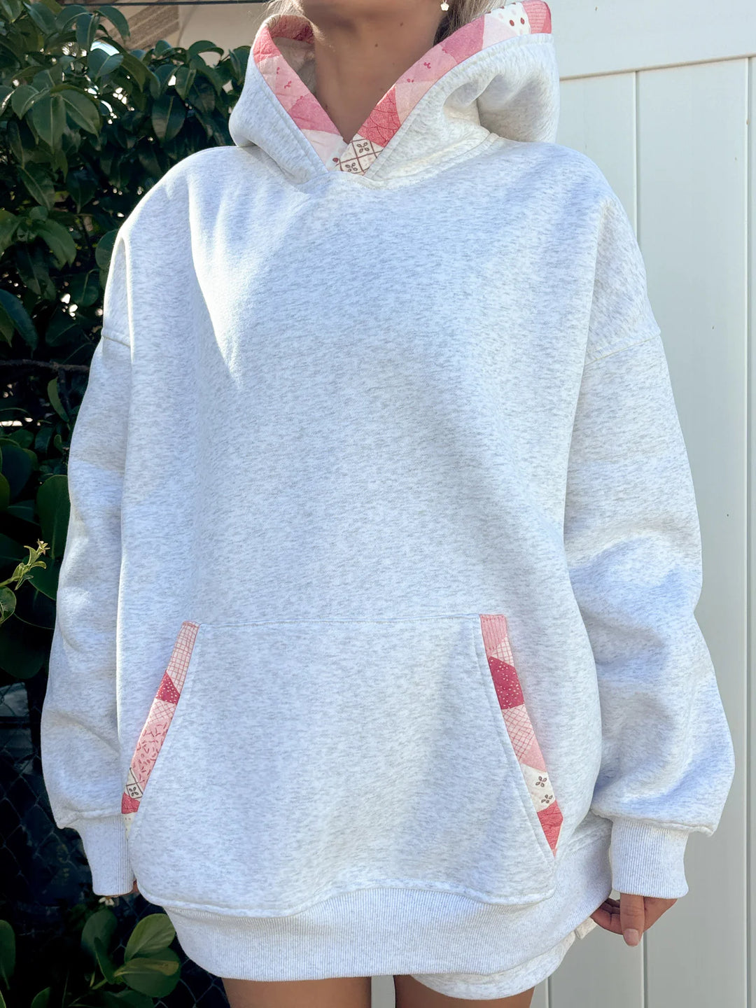 Person wearing grey sweatshirt with pink patchwork standing outdoors