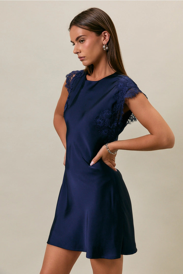 Woman wearing a navy blue dress with lace sleeves on a beige background