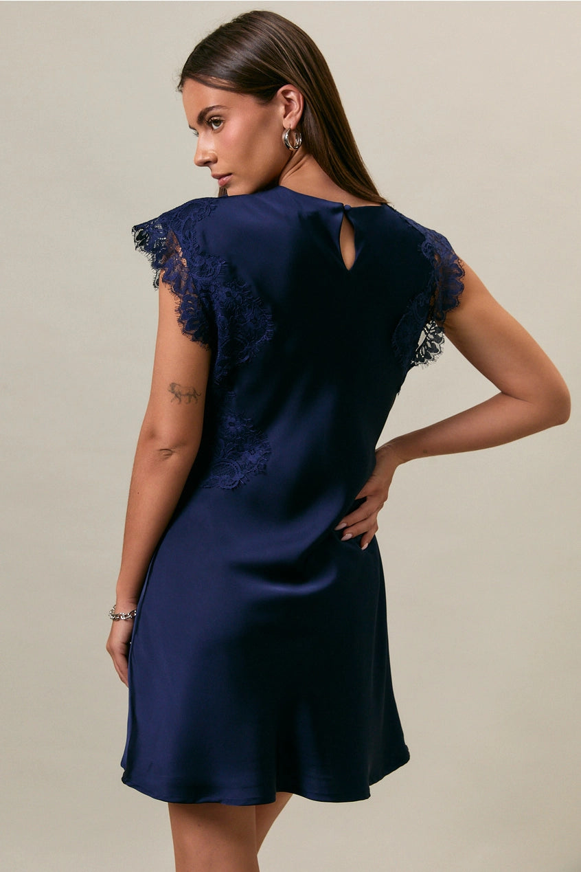 Woman wearing a navy blue dress with lace details on a beige background