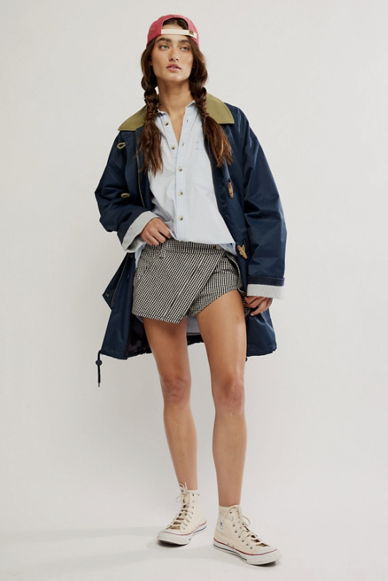 Person wearing a navy raincoat, white shirt, plaid shorts, and pink cap on a white background