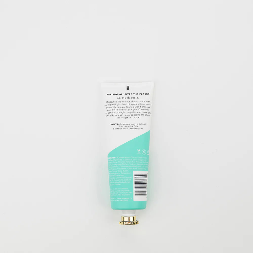 The back of a white plastic tube of hand wash with a metallic gold cap, featuring a mint green wave graphic and black text, set against a plain white background.
