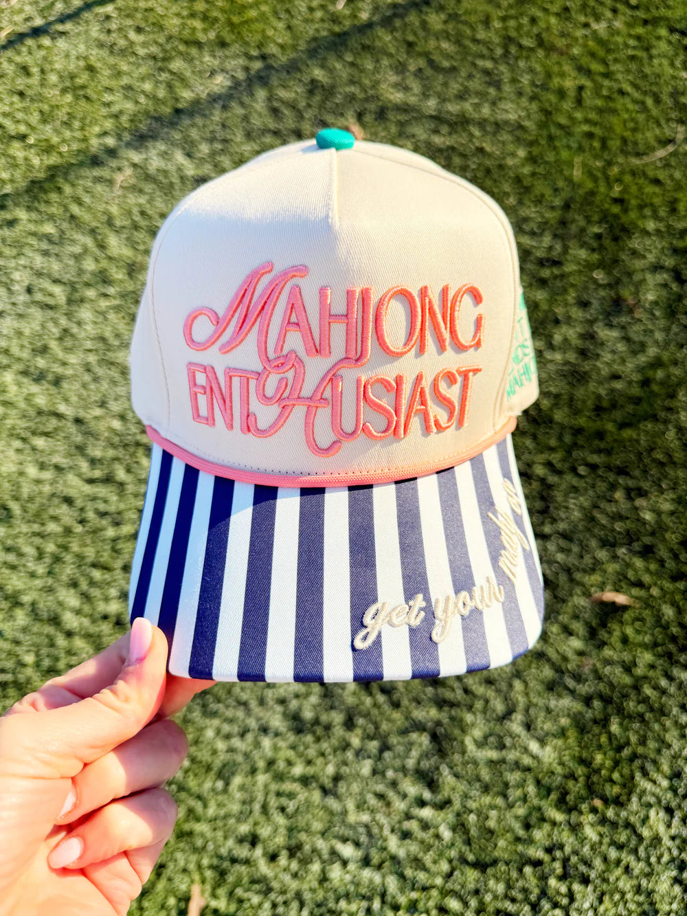 Cap with 'Mahjong Enthusiast' text held against a grass background