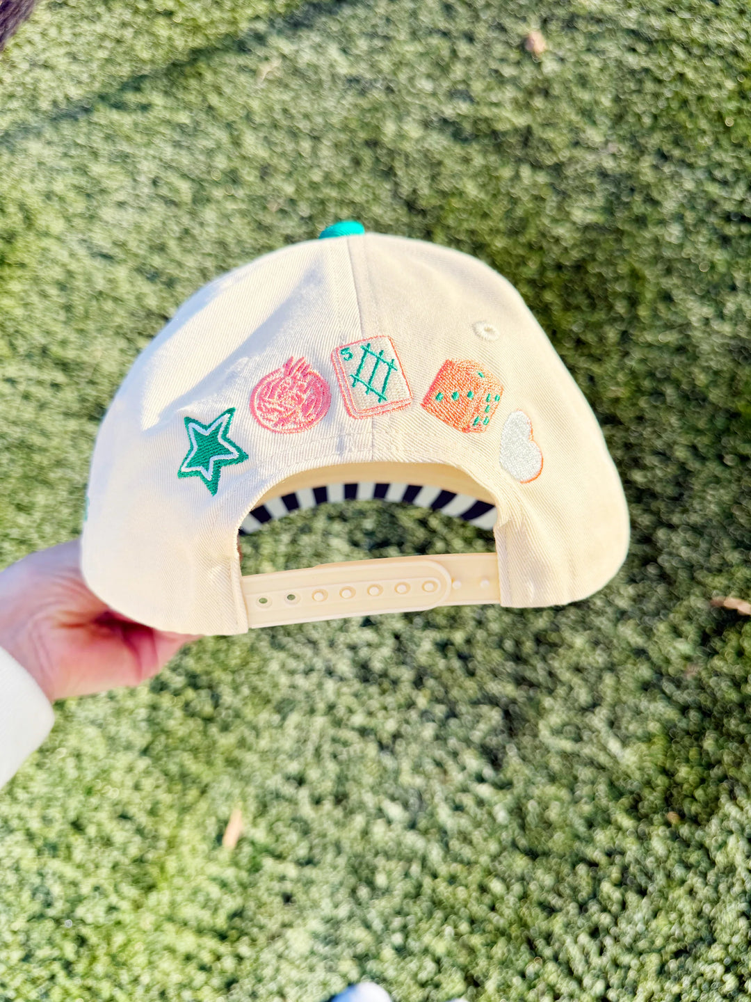 Beige cap with colorful patches held against a grassy background