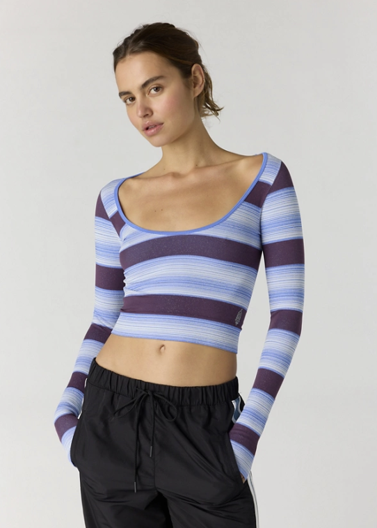 Woman wearing blue and purple stripe long sleeve top with black pants on plain background