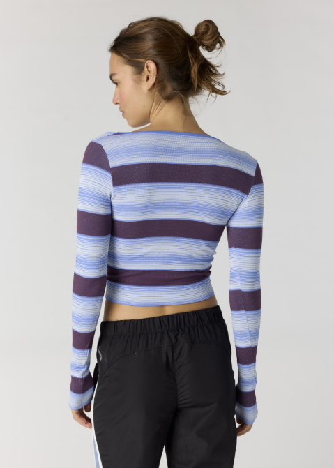 Woman shown from back wearing blue and purple stripe long sleeve top with black pants on plain background