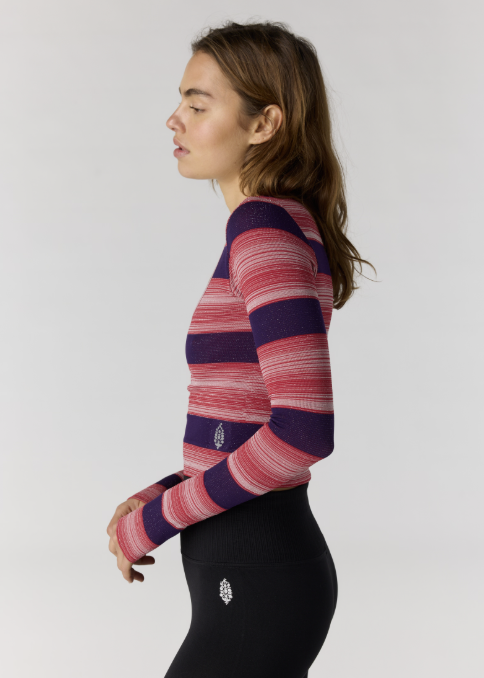 Woman wearing red and purple stripe long sleeve top with black leggings on plain background