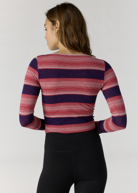 Woman shown from back wearing red and purple stripe long sleeve and black leggings on plain background