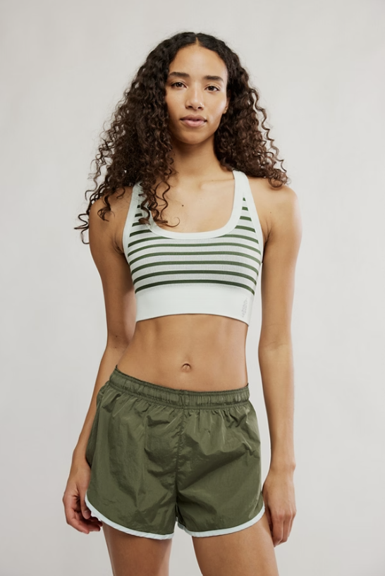 Woman wearing a striped sports bra and green shorts on a plain background