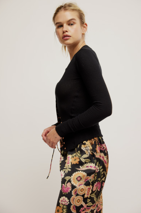 A woman modeling a black ribbed long-sleeve top paired with a black floral skirt, photographed against a plain light gray studio background.