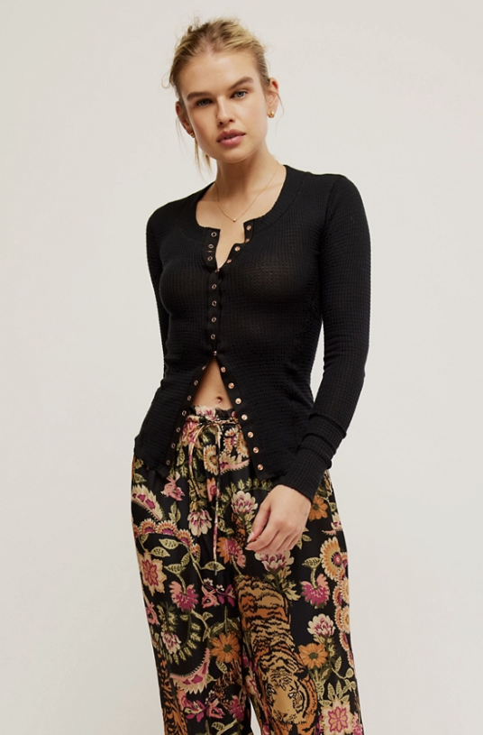 Woman wearing black cardigan and floral pants on white background