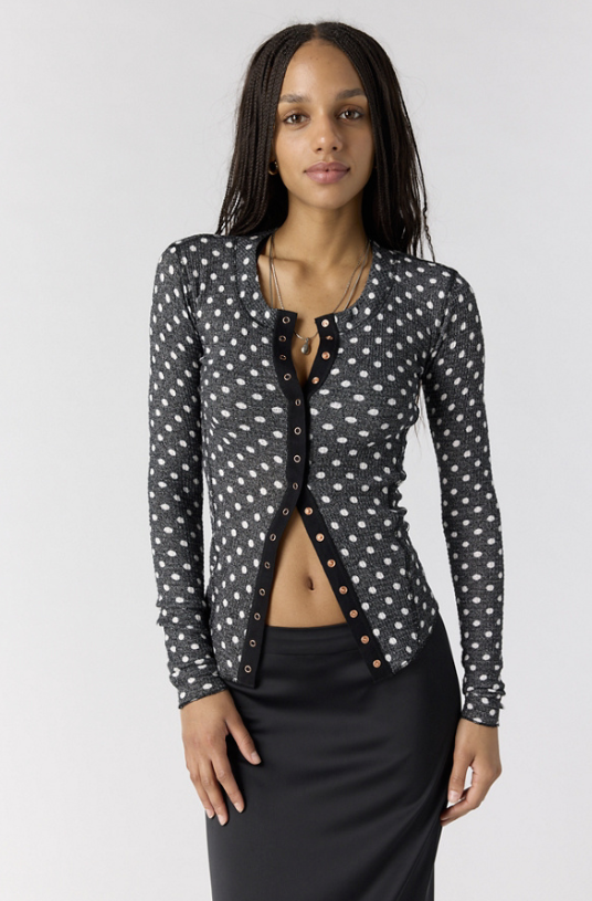 Woman wearing black cardigan with white polka dots and black skirt on white background