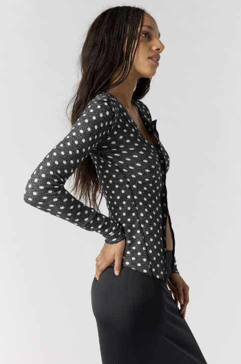 Woman wearing black cardigan with white polka dots and black skirt on white background
