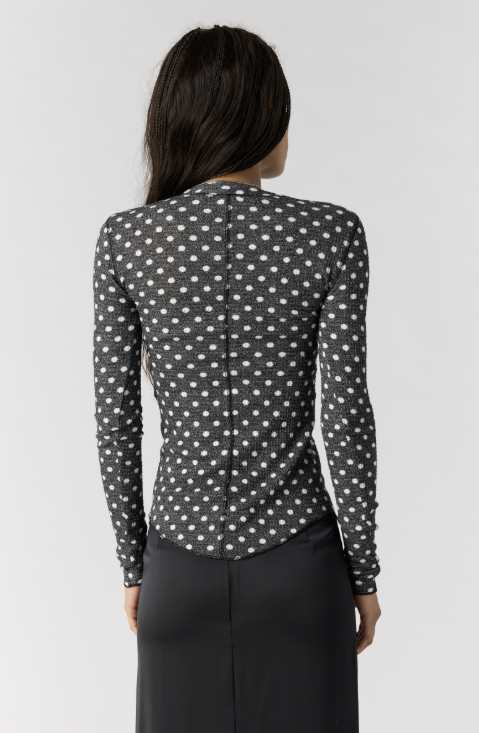Woman shown from back wearing black cardigan with white polka dots and black skirt on white background