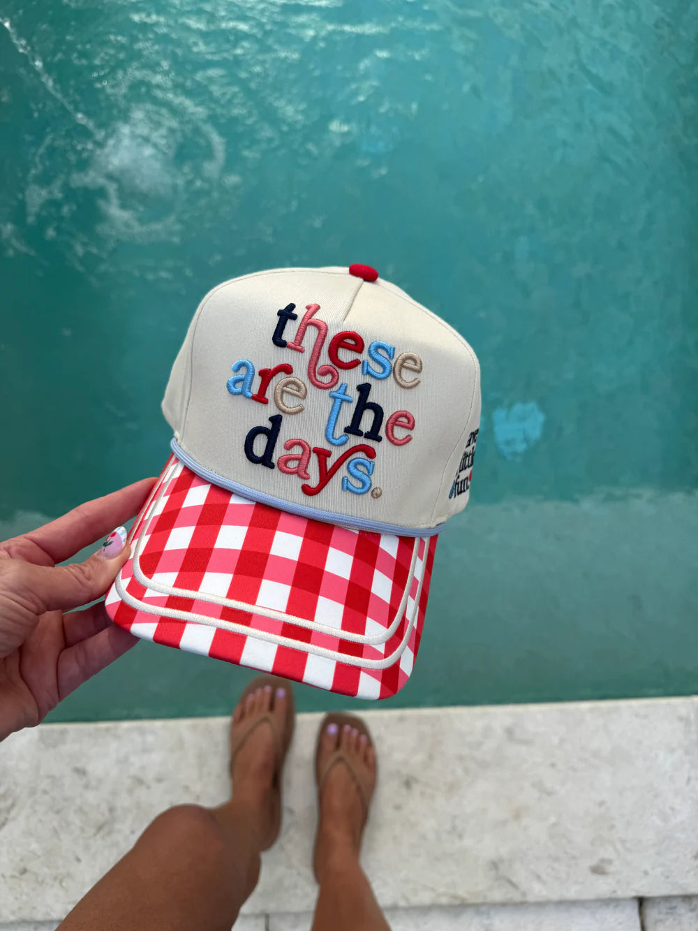 Cap with 'these are the days' text held by a person against a teal wall.