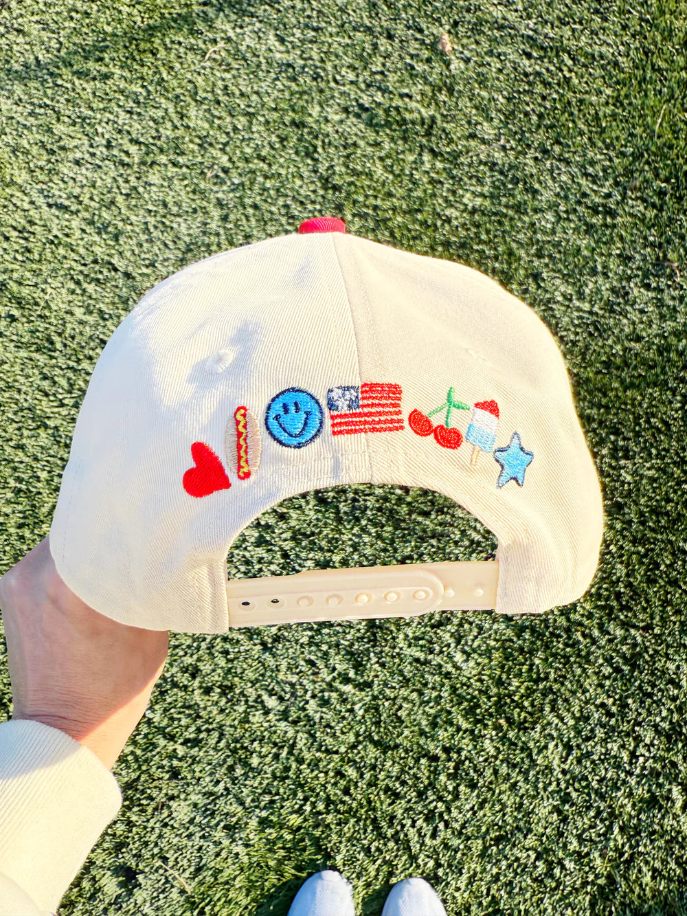 White cap with colorful embroidered designs held on a grassy background