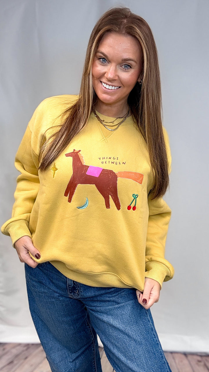 Woman wearing yellow sweatshirt with whimsical designs on plain background