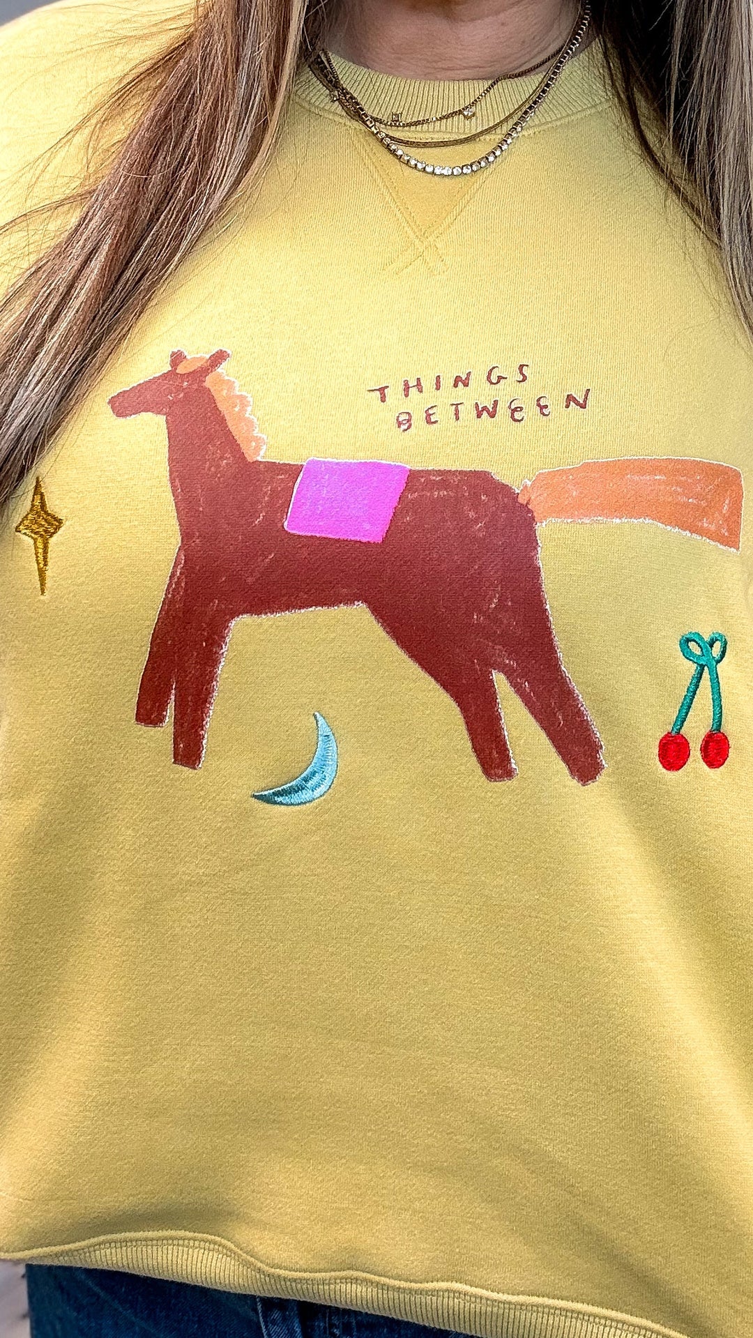 Woman wearing yellow sweatshirt with whimsical designs on plain background