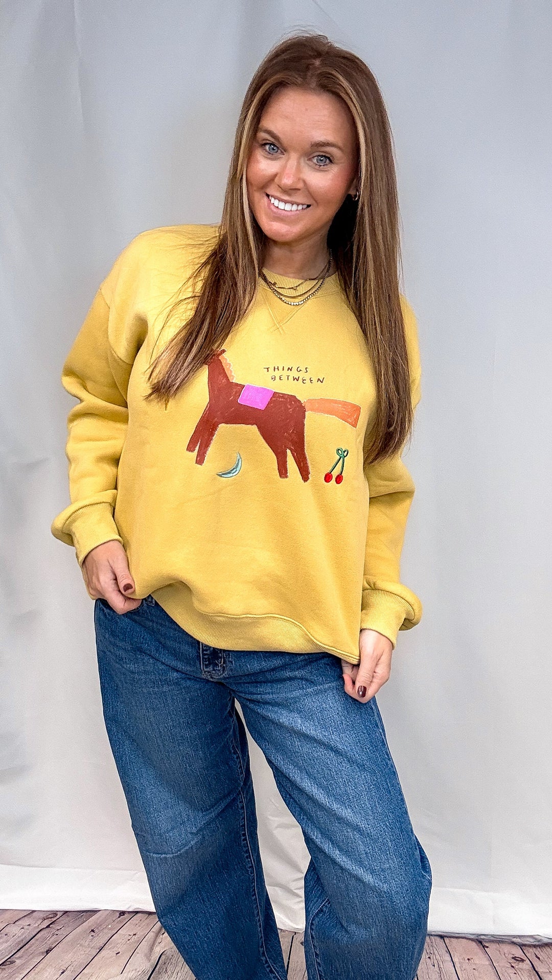 Woman wearing yellow sweatshirt with whimsical designs on plain background