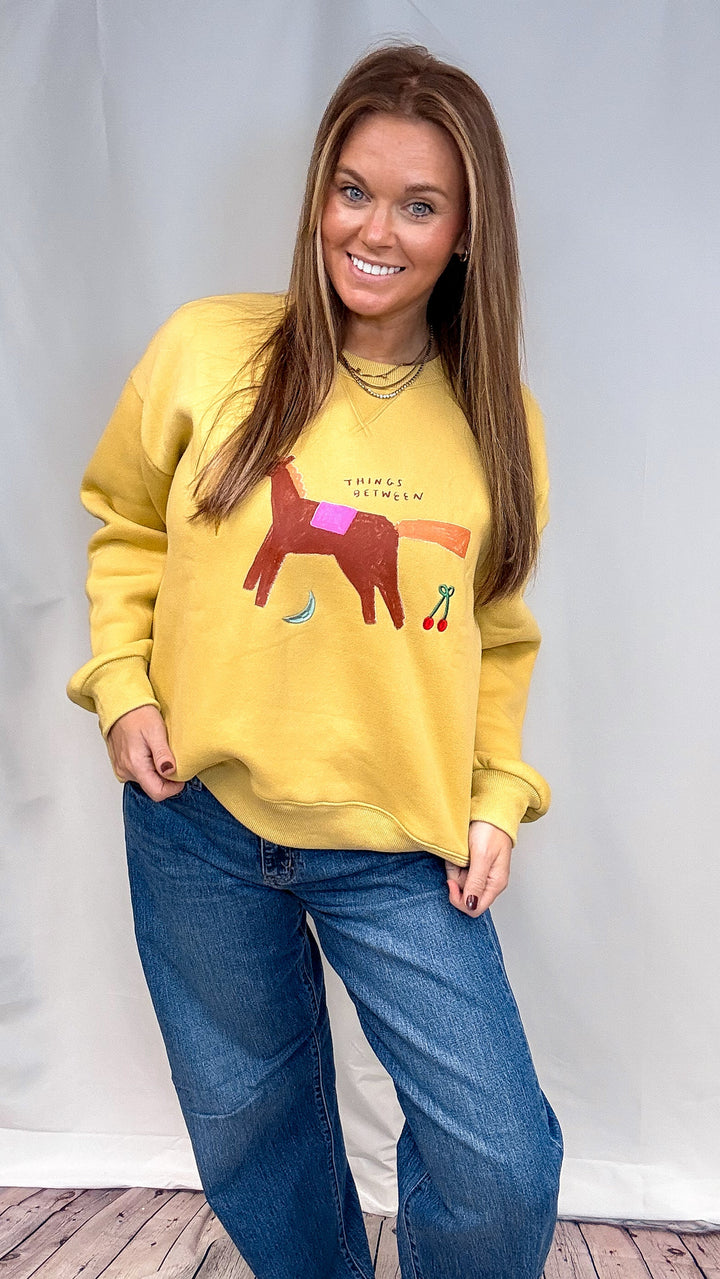 Woman wearing yellow sweatshirt with whimsical designs on plain background