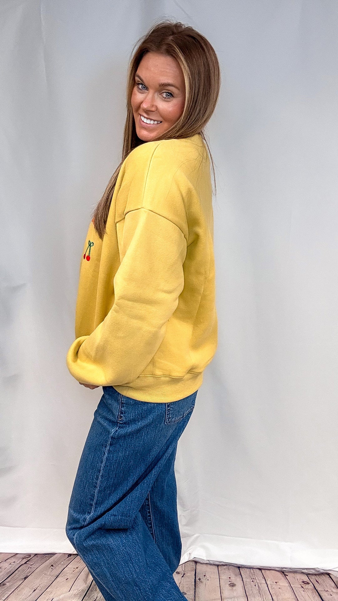 Woman wearing yellow sweatshirt and jeans on plain background